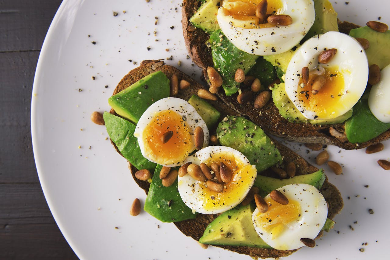 Delicious avocado toast topped with soft-boiled eggs and pine nuts on a white plate.